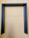 A black metal mounting frame or bracket with pre-drilled screw holes and textured inner slots, shown against a light brown corrugated cardboard background.