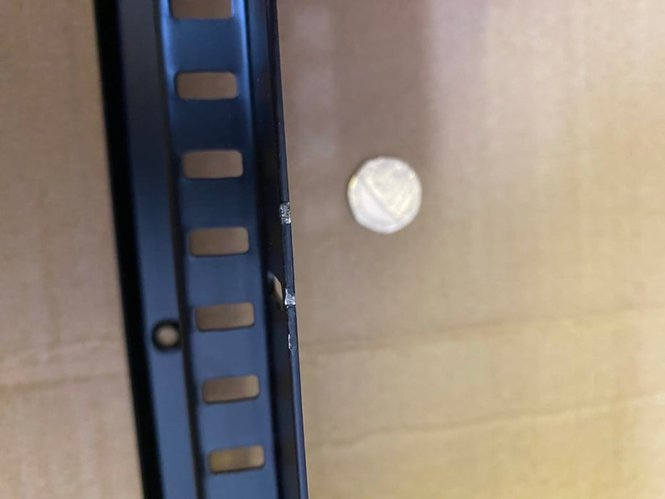 A close-up of a black metal shelving bracket next to a small white circular object on a brown cardboard background.