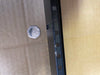 A close-up of a black metal mounting bracket or frame edge with rectangular cutouts, shown against a brown cardboard background with a small silver coin for scale.