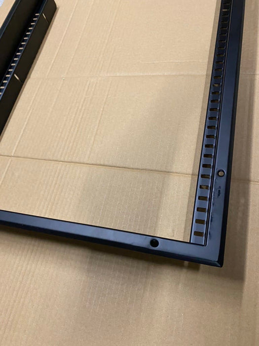 A close-up of a black metal frame corner with a slotted mounting channel, resting on a brown cardboard surface.