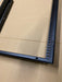 A close-up of a black metal frame corner with a slotted mounting channel, resting on a brown cardboard surface.