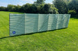 Blue Diamond 7-Pole Windbreak - Green Stripe, 5.4m - product image, showing windbreak pitched in open field with surrounding bushes