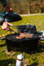 Cadac Citi Chef 40 Black - Urban & Camping Gas BBQ lifestyle image of burgers on the bbq getting flipped with tongs by hand, with other hand holder lid