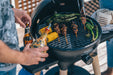 Cadac Citi Chef 40 FS Black - Urban & Camping Gas BBQ lifestyle image of close up of grill plate with veg and meat man's hand with oil bottle in and beer on side table with bread on other side table