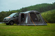 Vango Kela Pro Air Drive Away Awning - Low lifestyle image of awning pitched on VW camper  on grass with bushes and tress in background. both mesh doors zipped up but the main doors rolled up. 