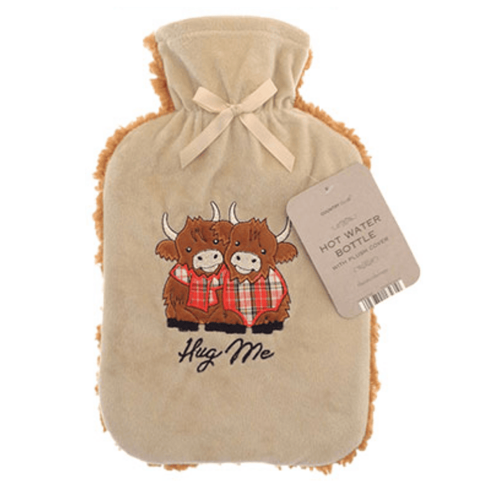 Country Club Hug Me Highland Cows 2L Sherpa Fleece Hot Water Bottle - main product image, showing a beige hot water bottle cover with a drawstring closure and fringed edges, featuring an embroidered design of two Highland cows in red plaid with the words 'Hug Me' below. A paper hangtag is attached on the right side.