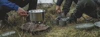 Easy Camp Moss 4 Person Camping Cook Set - lifestyle image, showing people cooking with pot over camping stove with mugs and plates