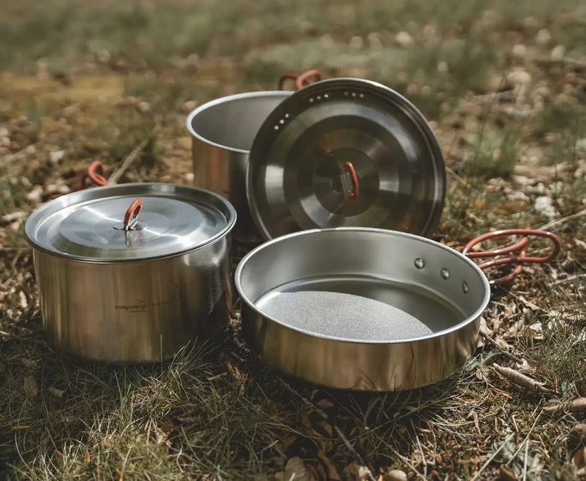 Easy Camp Moss Tour Stainless Steel Cook Set - lifestyle image, showing low side view of set components (2x pots with lids, 1x pan) outside on ground