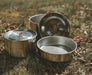 Easy Camp Moss Tour Stainless Steel Cook Set - lifestyle image, showing low side view of set components (2x pots with lids, 1x pan) outside on ground