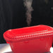 Heat 2 Eat, Medium Self Steamer Red container with steam rising from it against a black background