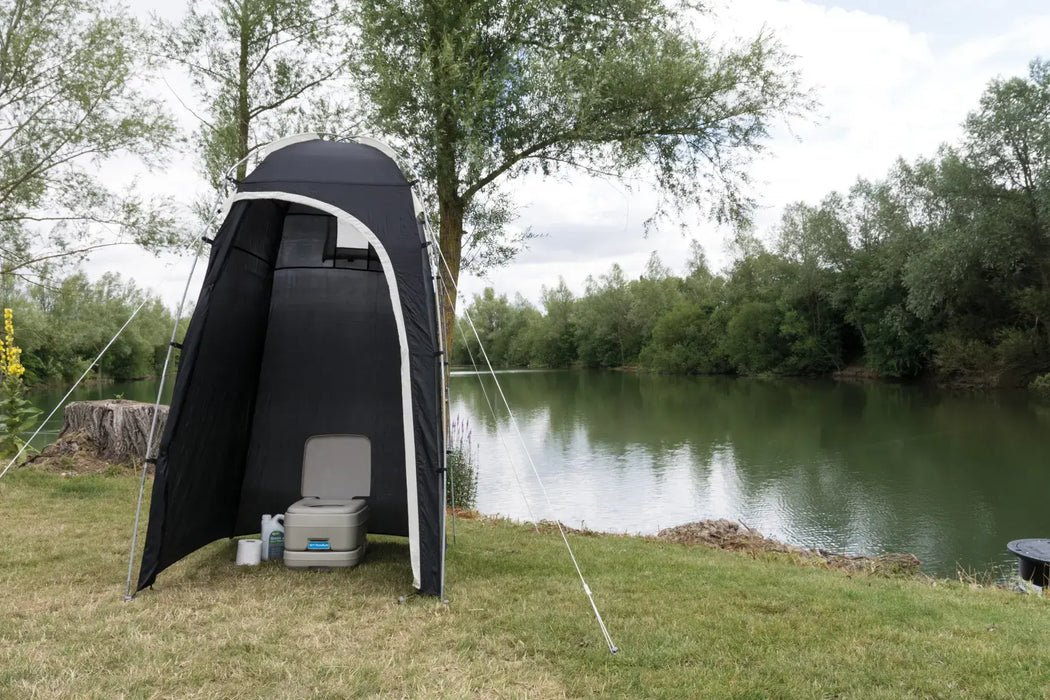 Kampa Loo-Loo Camping Toilet and Shower Tent - lifestyle image, showing tent with door open and camping toilet, chemical fluid and toilet roll inside, pitched  outside next to river and trees