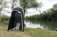 Kampa Loo-Loo Camping Toilet and Shower Tent - lifestyle image, showing tent with door open and camping toilet, chemical fluid and toilet roll inside, pitched  outside next to river and trees
