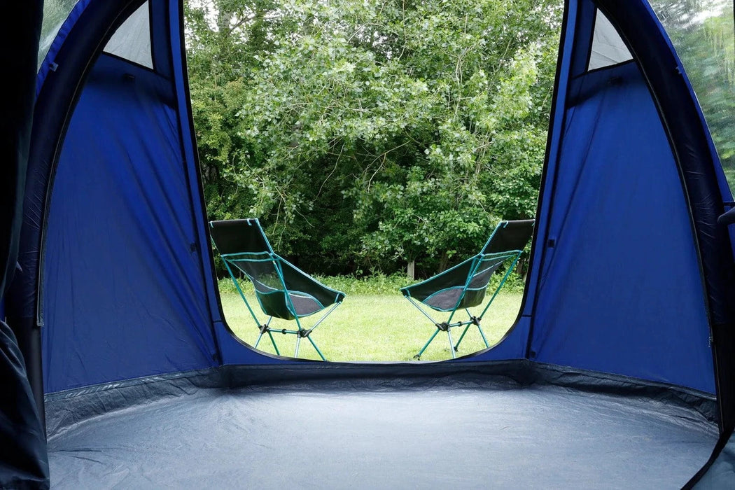 Camping scene with a blue tent, chairs, and greenery outside.