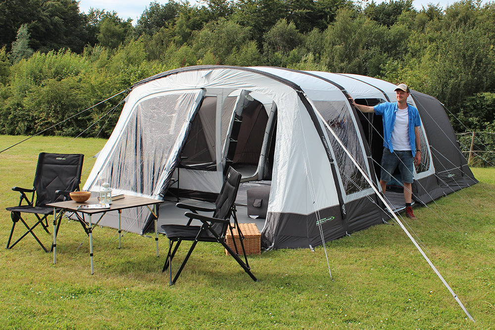Outdoor Revolution Airedale 6S Inflatable Tent 2024 - 6 Berth Tunnel Tent feature image of tent pitched on campsite. man coming out of right side door, table and chairs in front of front porch with picnic basket on ground. all curtains unzipped