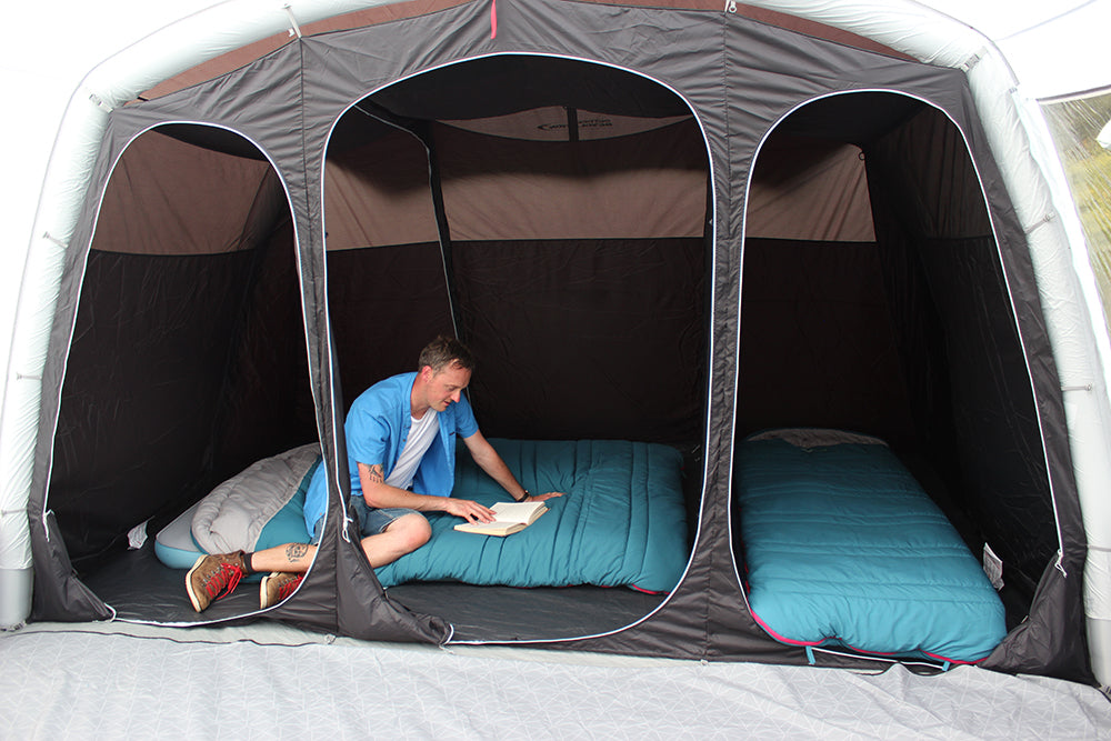 Outdoor Revolution Airedale 6S Inflatable Tent 2024 - 6 Berth Tunnel Tent feature image of bedroom compartments, with left divider down and a double bed side ways with man sitting on bed and sleeping bag. right bedroom set up with single bed with blue sleeping bag