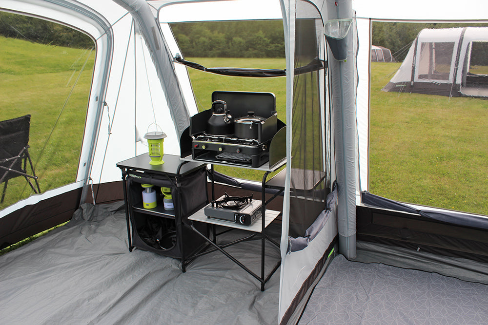 Outdoor Revolution Airedale 6S Inflatable Tent 2024 - 6 Berth Tunnel Tent feature image of tent pitched on campsite. showing front porch areas with dividing door open and curtain rolled down to see mesh. kitchen stand set up below window