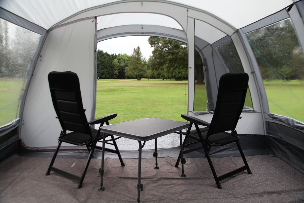 Outdoor Revolution Camp Star 600 DT- Poled 6-Berth Tunnel Tent Bundle lifestyle image of pitched on campsite with trees surrounding. image from inside the tent living space looking out with 2 chairs and a table in the foreground of the main living area