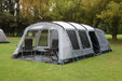 Outdoor Revolution Camp Star 600 DT- Poled 6-Berth Tunnel Tent Bundle lifestyle side view image of tent pitched on campsite with trees surrounding. image shows right side of tent with all doors open. and windows clear. 2 chairs and a table sit in front porch area and you can see the divide into the second living space. 