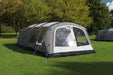 Outdoor Revolution Camp Star 600 PC DT- Polycotton Poled 6-Berth Tunnel Tent Bundle image of the tent pitched on a campsite surrounded by green trees.  left side view of tent with front door zipped up