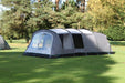 Outdoor Revolution Camp Star 600 PC DT- Polycotton Poled 6-Berth Tunnel Tent Bundle image of the tent pitched on a campsite surrounded by green trees.  right side view of tent with door zipped up and front door zipped up both window panels on front right without curtains toggled up