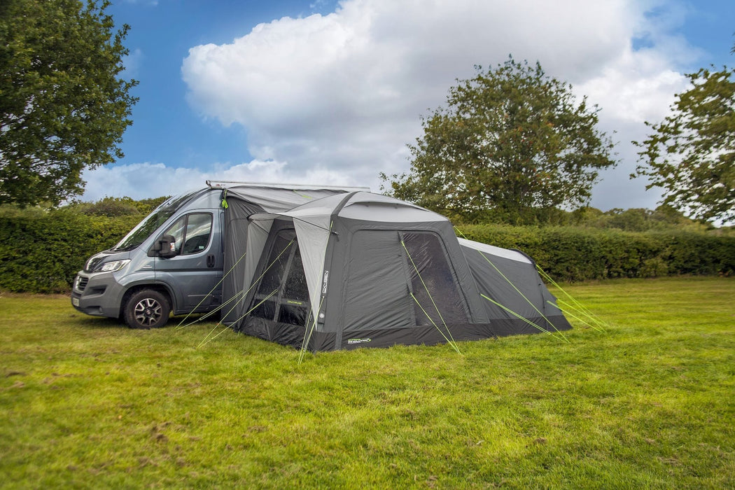 orda1623-05 Gray caravan with an extended awning in a grassy area with trees and blue sky.