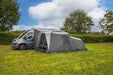 orda1623-05 Gray caravan with an extended awning in a grassy area with trees and blue sky.