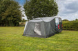 orda1623-11 Caravan with an extended awning in a grassy area with trees and a cloudy sky.