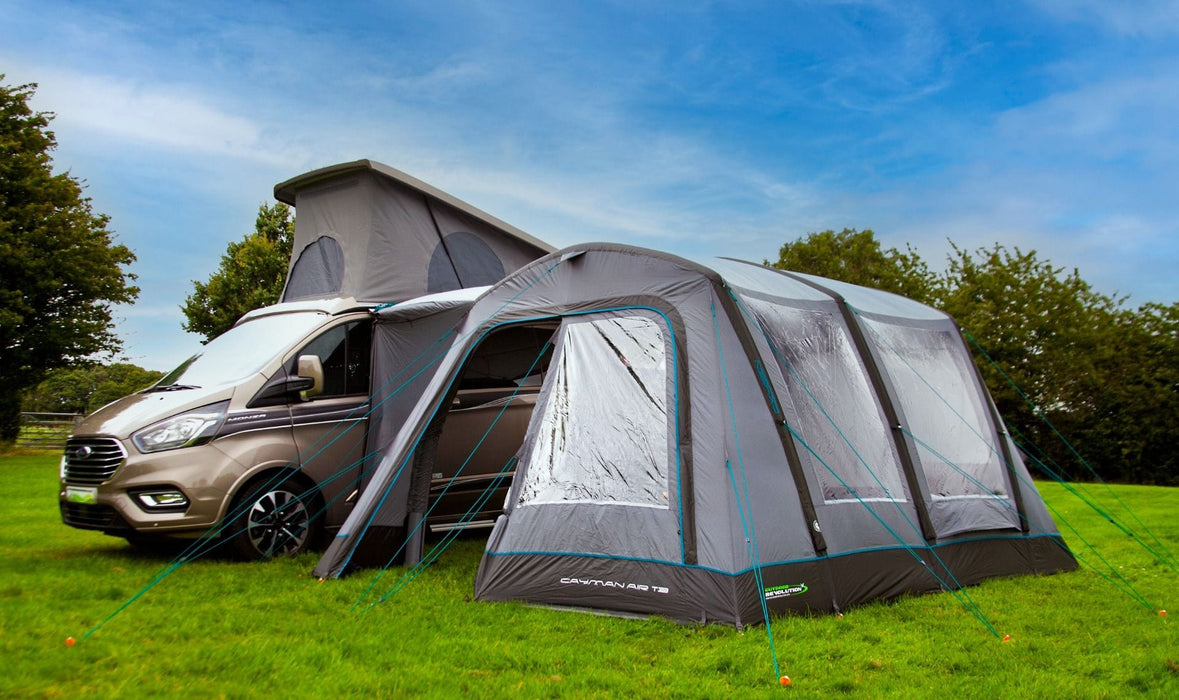 Van with an attached caravan tent on a grassy area with trees in the background