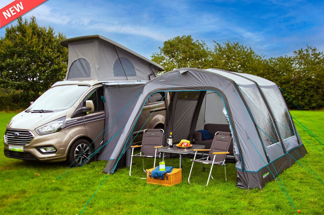 Van with a large awning extended on a grassy area with trees in the background
