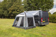 Van with a gray and black awning extended outdoors on a grassy area with trees in the background.