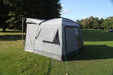 Outdoor Revolution Cuda (F/G) Low Drive Away Awning Feature image of the awning pitched on campsite grass with green trees surrounding. Left side view of small vented window and pitched on frame showing cowl up. 