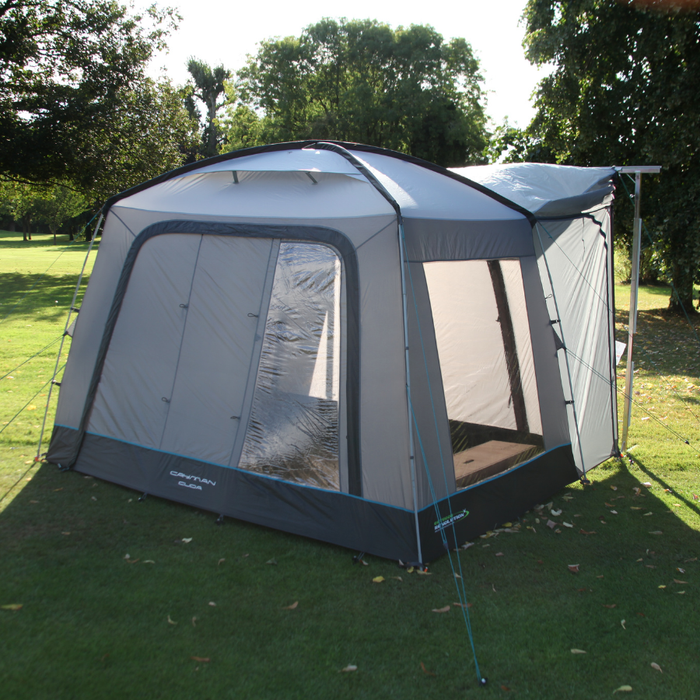 Outdoor Revolution Cuda (F/G) Low Drive Away Awning Feature image of the awning pitched on campsite grass with green trees surrounding.  right side view of awning pitched against frame with cowl up. Sun shining throwing shadow in front of the awning. 