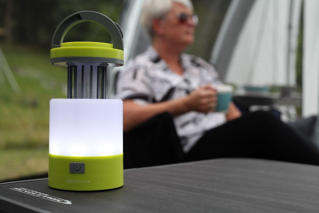 Outdoor Revolution Lumi-Mosi Recharageable Lantern & Mosquito Killer - lifestyle image, showing lit lantern, with mosi-killer compartment extended, sat on table outside with person sat in background