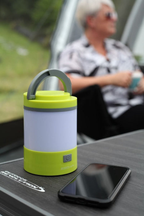 Outdoor Revolution Lumi-Mosi Recharageable Lantern & Mosquito Killer - lifestyle image, showing unlit lantern, without mosi-killer compartment extended, sat on table outside next to smart phone, with person sat in background