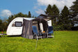 Outdoor Revolution Porch Pro 260 Inflatable Caravan Awning - product image, showing awning pitched and attached to caravan in a field surrounded by trees, with front door raised open as a canopy, with chairs and table in front of awning