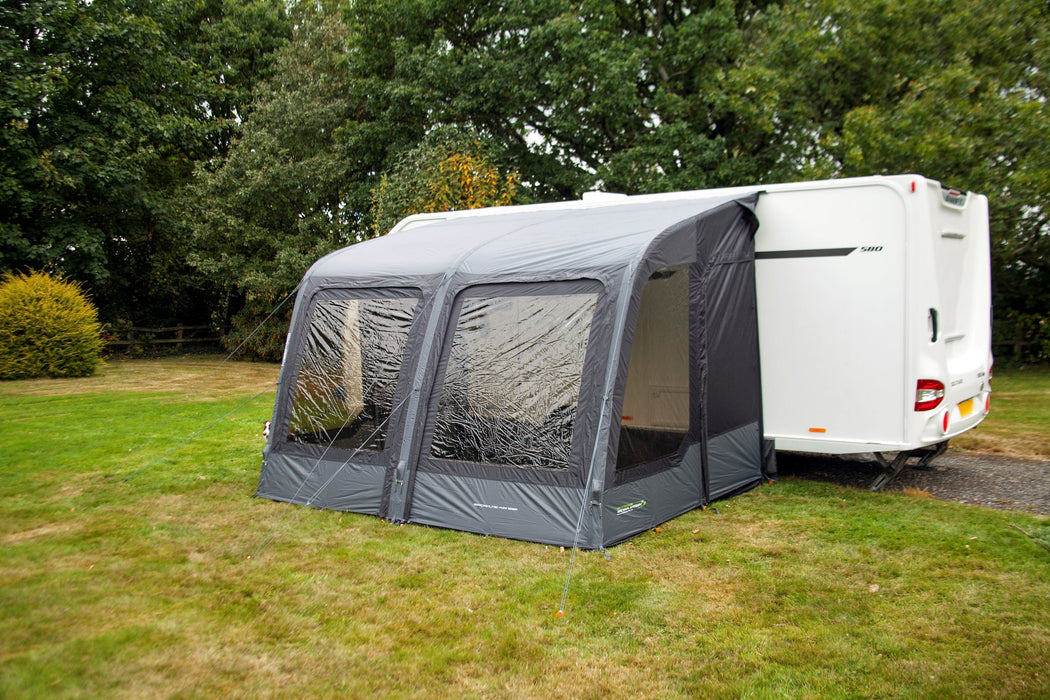 Outdoor Revolution Sport Lite Air 330 Inflatable Caravan Awning - product image, showing front-right side view of awning attached to caravan pitched in field with surrounding trees and bushes