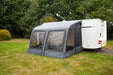Outdoor Revolution Sport Lite Air 330 Inflatable Caravan Awning - product image, showing front-right side view of awning attached to caravan pitched in field with surrounding trees and bushes