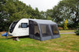 Outdoor Revolution Sport Lite Air 330 Inflatable Caravan Awning - product image, showing front-left side view of awning attached to caravan pitched in field with surrounding trees, and dog lying on grass to left-hand side of awning