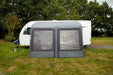 Outdoor Revolution Sport Lite Air 330 Inflatable Caravan Awning - product image, showing front-on view of awning attached to caravan pitched in field with surrounding trees, and dog lying on grass to left-hand side of awning
