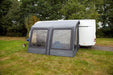 Outdoor Revolution Sport Lite Air 330 Inflatable Caravan Awning - main product image, showing front-right side view of awning attached to caravan pitched in field with surrounding trees, and dog lying on grass to left-hand side of awning