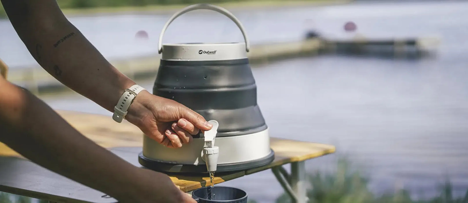 Outwell Collaps 6 Litre Camping Water Carrier - lifestyle image, showing person using tap to pour water into cup