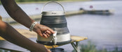 Outwell Collaps 6 Litre Camping Water Carrier - lifestyle image, showing person using tap to pour water into cup