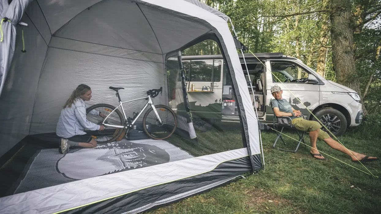 Outwell Dakota Freestanding Outdoor Camping Shelter - lifestyle image, showing couple using shelter with front and side doors open, next to motorhome