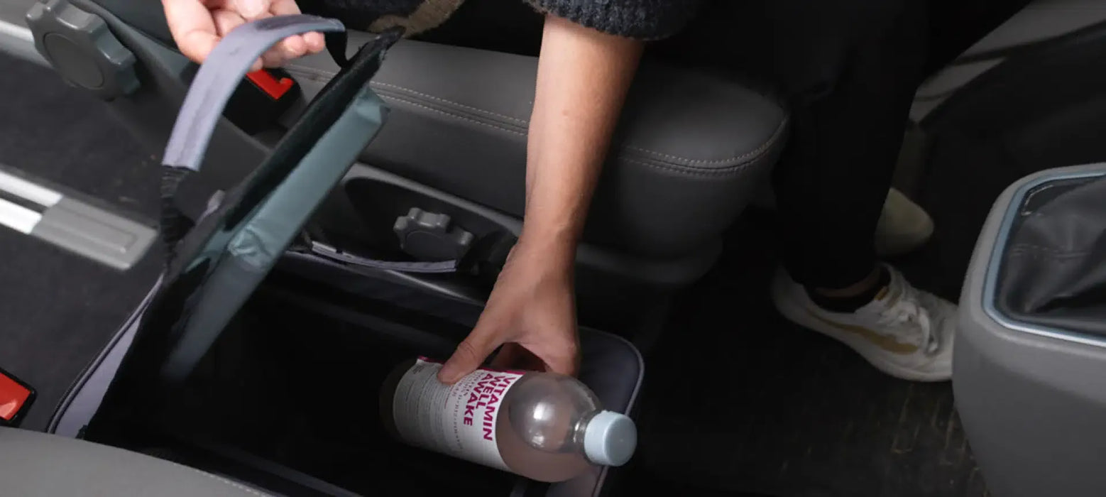 Outwell Eagle Van Cooler 15 Litre Camping Cool Bag - lifestyle image, showing person putting bottle into cool bag placed between seats inside a vehicle