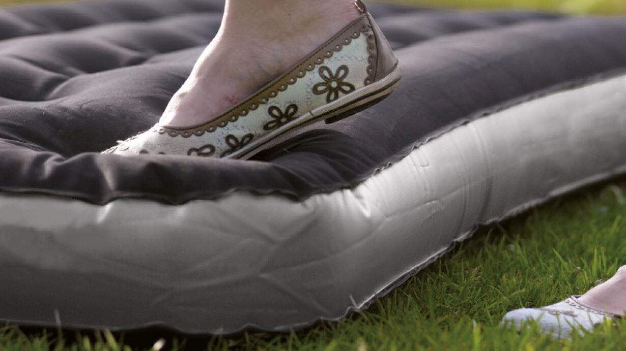 Outwell Flock Classic Single Airbed with Pillow & Pump feature image of a foot pushing down on side corner of airbed whilst on grass