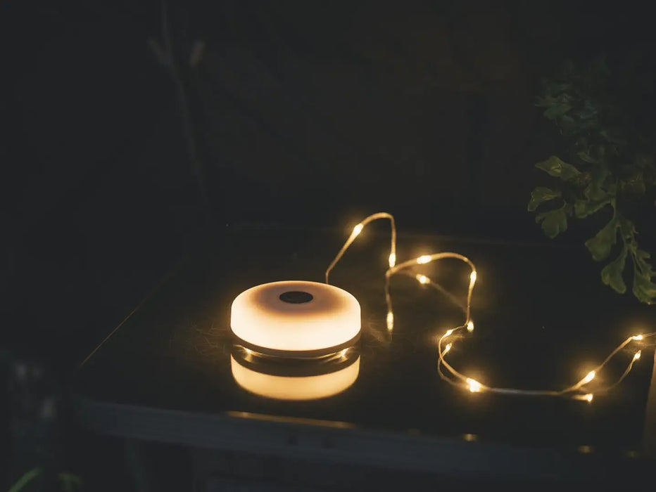 Outwell Moonstone String Light Camping Lantern - lifestyle image, showing light and string lights around plant pot