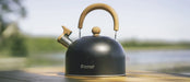 Outwell Tea Break Lux 1.8 Litre Camping Kettle - lifestyle image, showing kettle on table surface outdoors