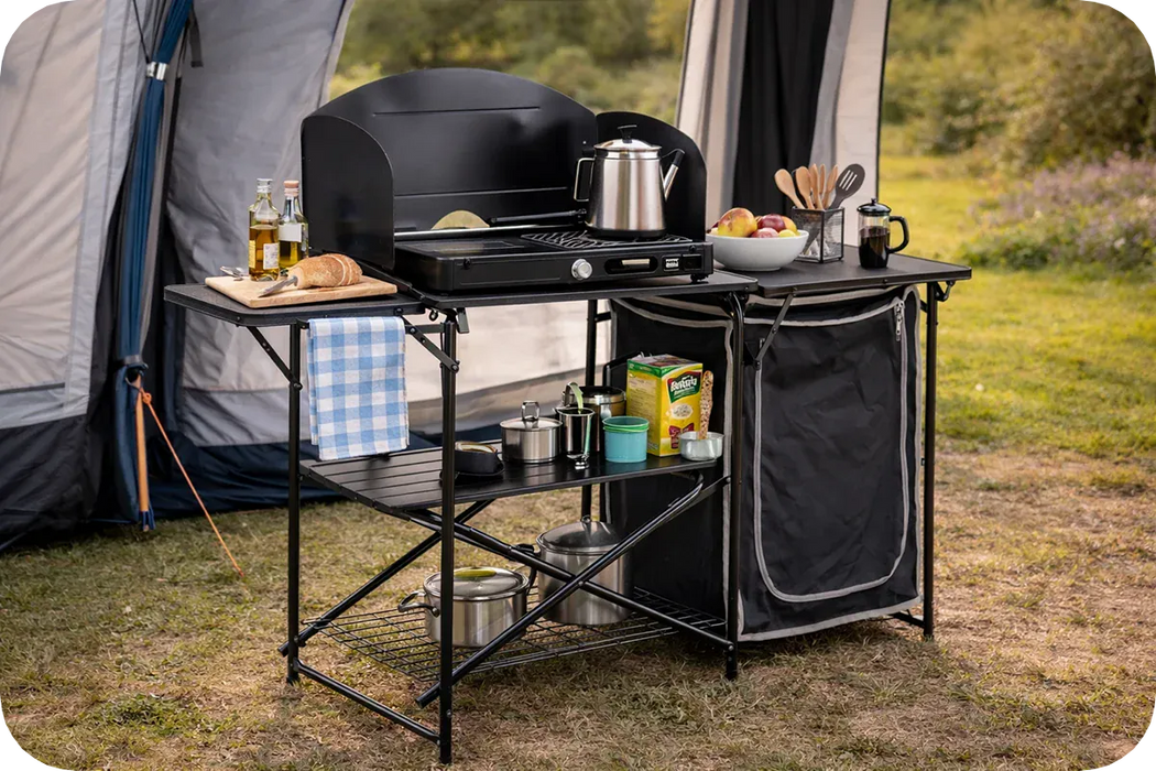 Quest Oregano Folding Camping Kitchen Stand with Storage – lifestyle image, showing unit being used in outdoor environment with awning behind