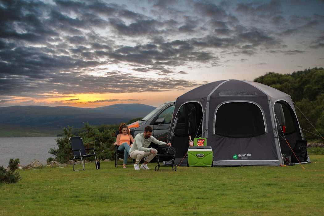 Vango Airhub Hexaway Pro Drive Away Awning Low - Cloud Grey lifestyle image of a couple having a bbq outside awning with doors open, lake mountain and sunset in background