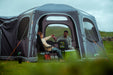 Vango Airhub Hexaway Pro Drive Away Awning Low - Cloud Grey lifestyle image of awning iwht door open and couple sitting sharing food with coolbox on the floor